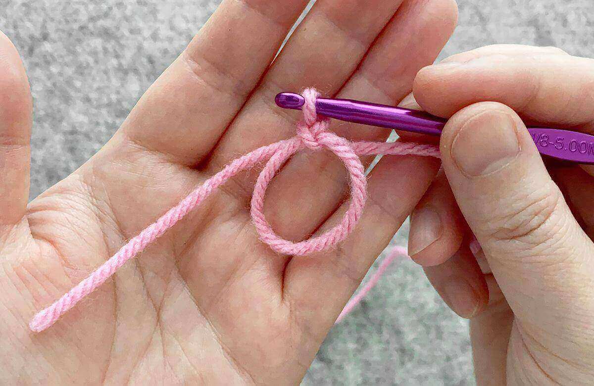 Mãos fazendo anel mágico no crochê com fio rosa e agulha